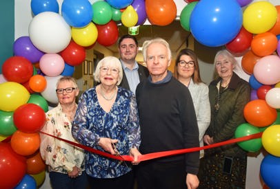 People standing cutting ribbon with balloons.